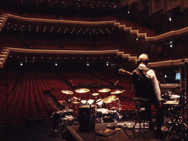 Robert Fripp stands on an empty stage