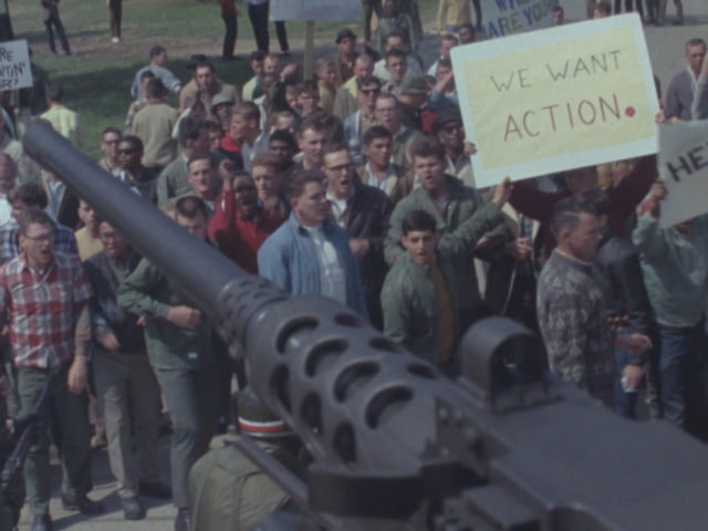 Archive image from 'Riotsville', a group of people seemingly protesting in frint of a tank.